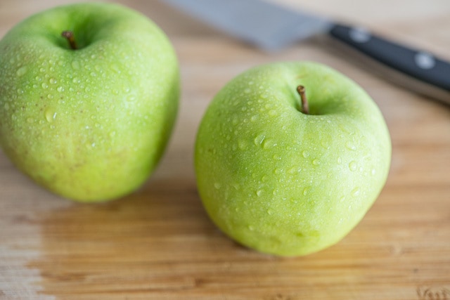 A green apple on top of a wooden cutting board